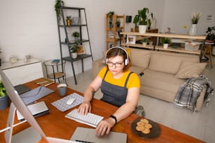 Concentrated young female programmer sitting in wheelchair and using computers while working at home