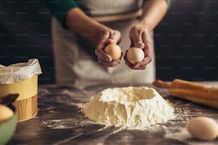 Hands breaking egg into raw dough on wooden table.