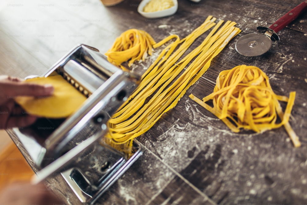 Zubereitung von hausgemachter Pasta mit Nudelmaschine auf Holztisch.