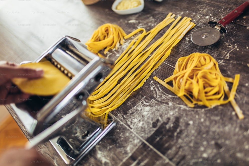 Zubereitung von hausgemachter Pasta mit Nudelmaschine auf Holztisch.