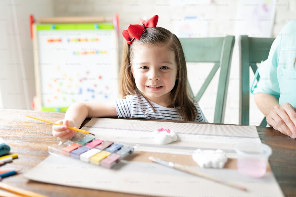 Cute little three year old using watercolors to paint a plaster cupcake figure and enjoying homeschool with her mom