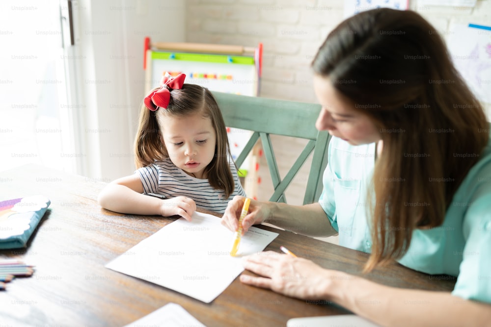 Mutter erklärt eine Aktivität und gibt ihrer kleinen Tochter Anweisungen, während sie unterrichtet und zu Hause unterrichtet