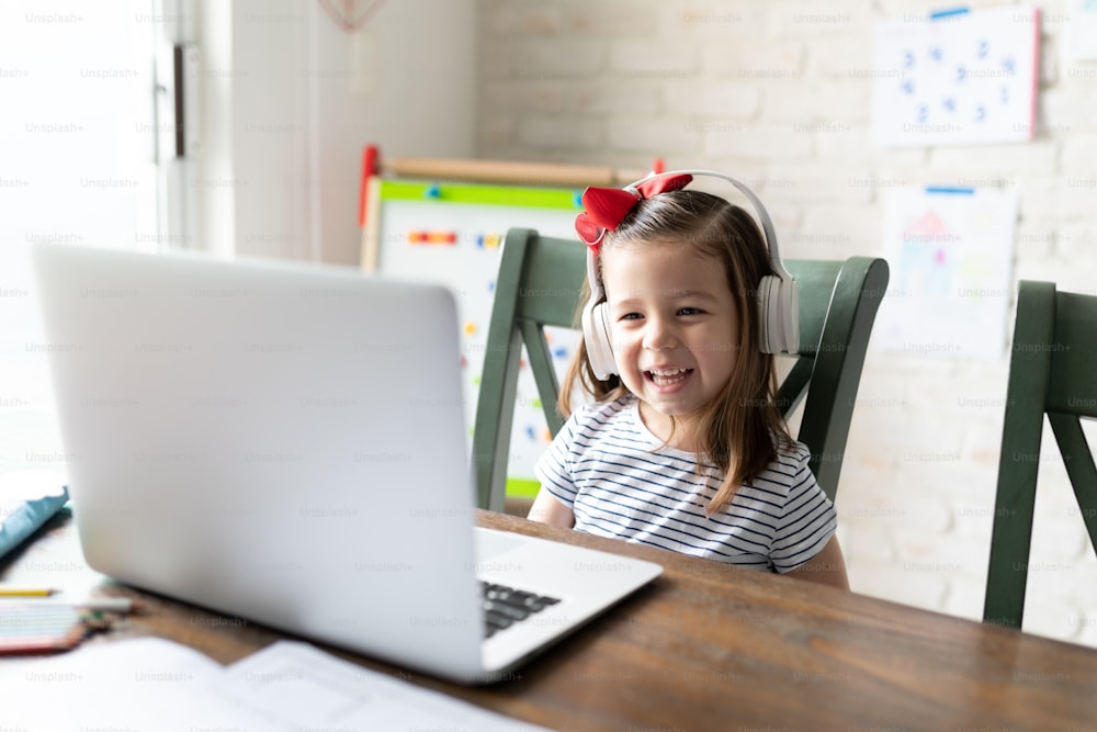 Nettes kaukasisches Kleinkind, das Kopfhörer trägt und lacht, während es sich zu Hause etwas Lustiges auf einem Laptop ansieht
