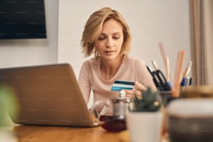 Front view of a focused blonde pretty lady staring at a card in her hand