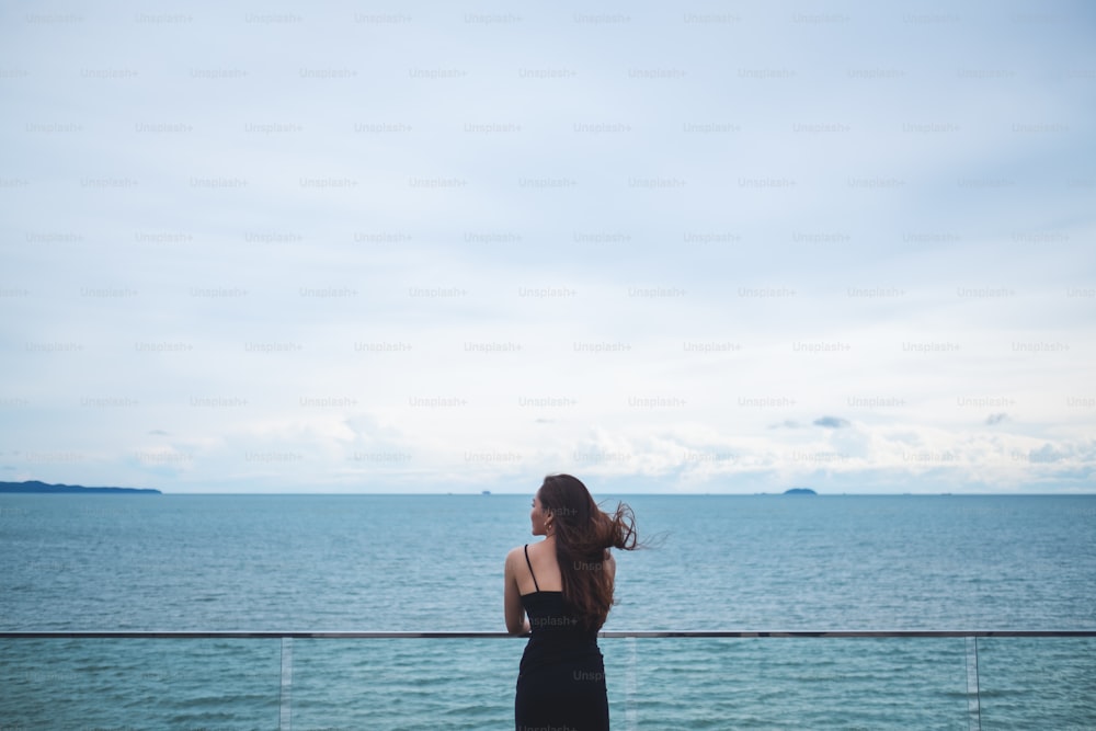 Imagem retrovisora de uma bela jovem mulher asiática em pé e olhando para o mar e o céu azul