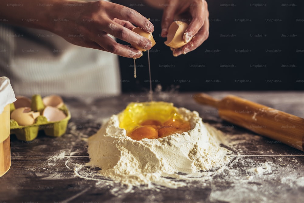 Mani che rompono l'uovo in pasta cruda su un tavolo di legno.