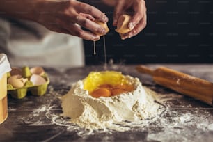 Hands breaking egg into raw dough on wooden table.