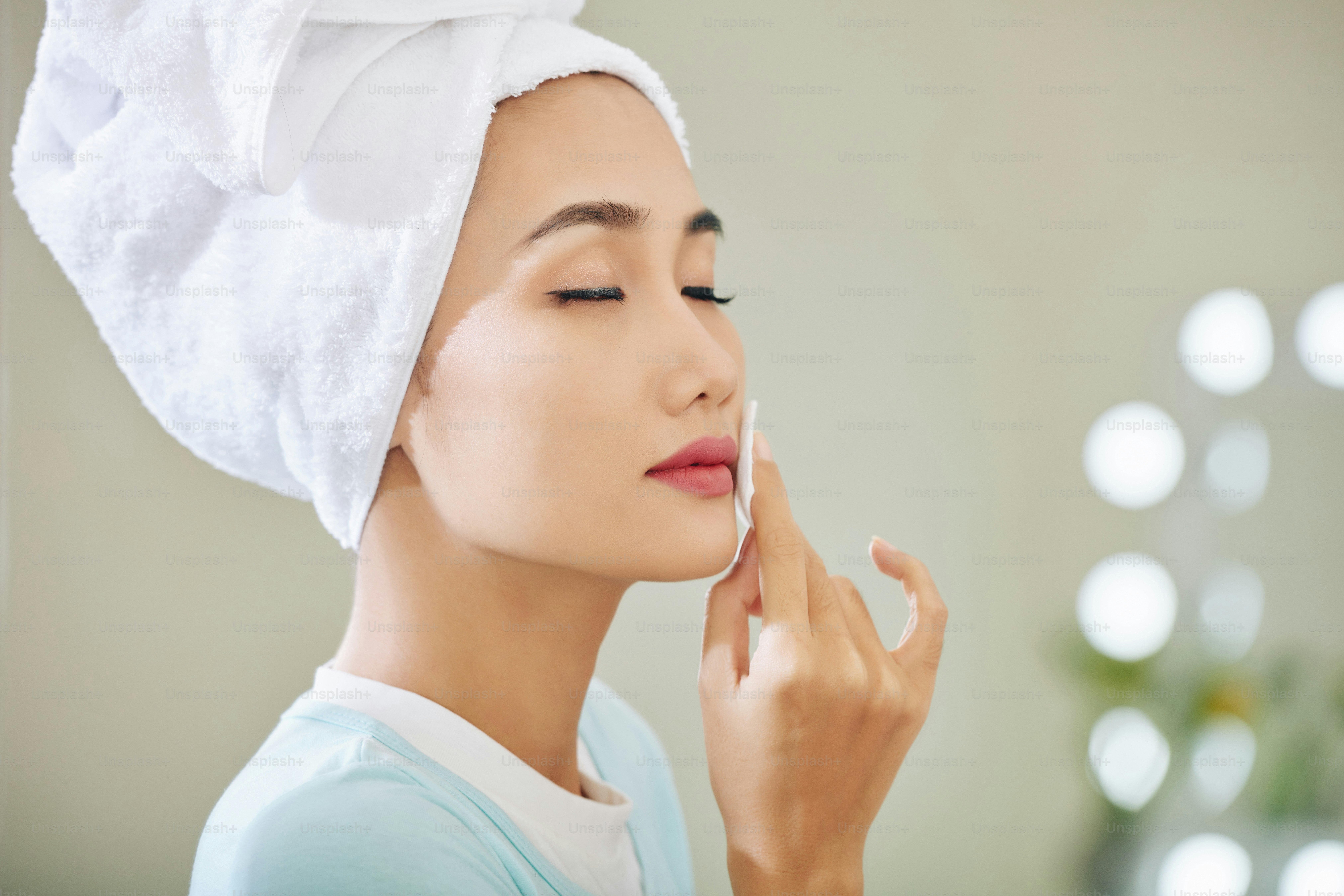 Beautiful young Asian woman closing eyes when wiping off lipstick with micellar water on cotton pad