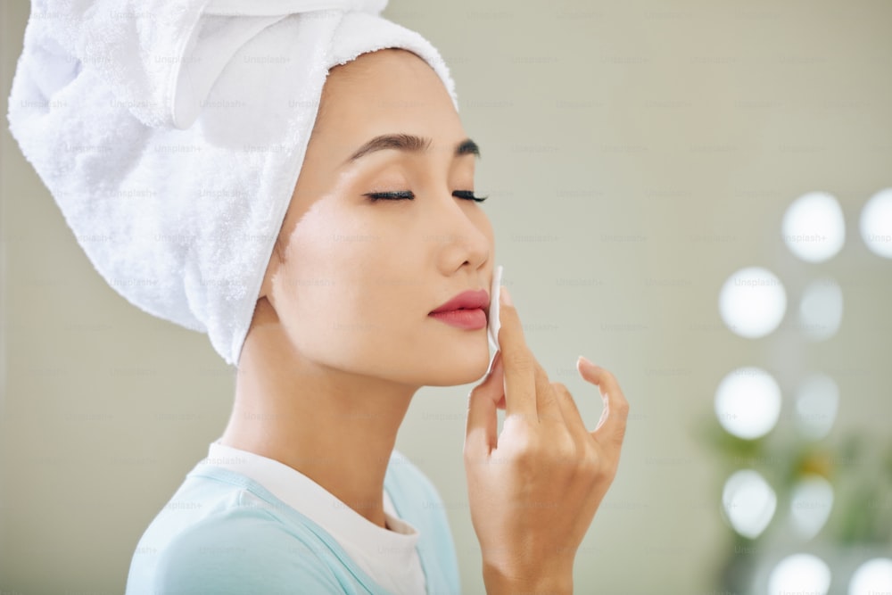아름 다운 젊은 아시아 여자는 화장솜에 미셀라 물로 립스틱을 닦을 때 눈을 감고 있습니다