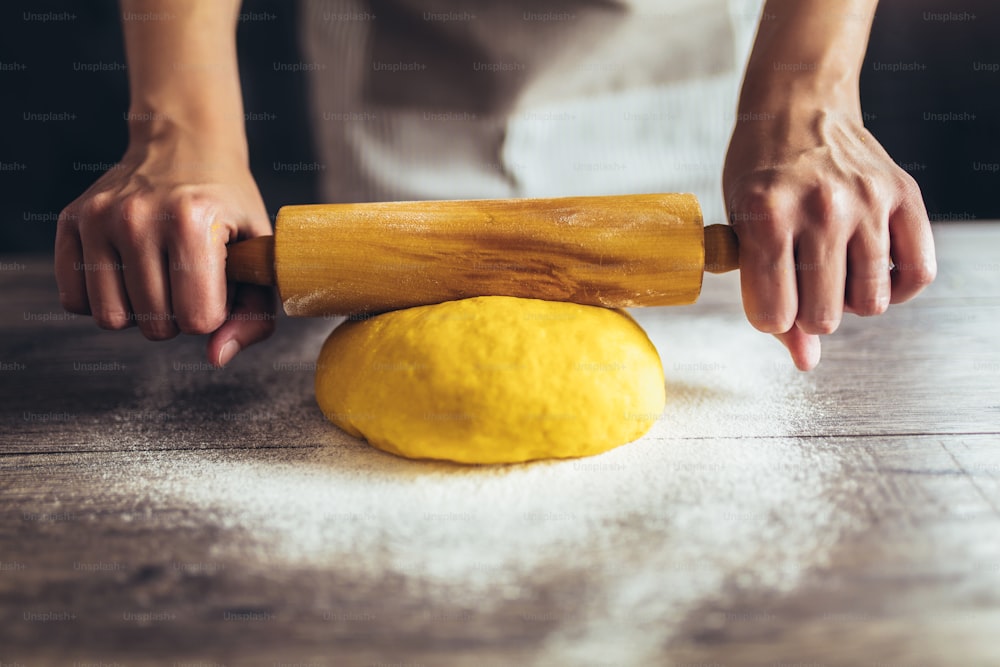 Cuisine maison, les mains féminines roulent les pâtes avec un rouleau à pâtisserie sur une table en bois.