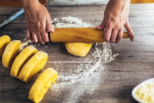 Woman rolled out pasta dough on the table with the rolling pin.