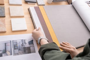 Hands of young contemporary designer looking through samples of wallpapers for walls of room of new house or apartment