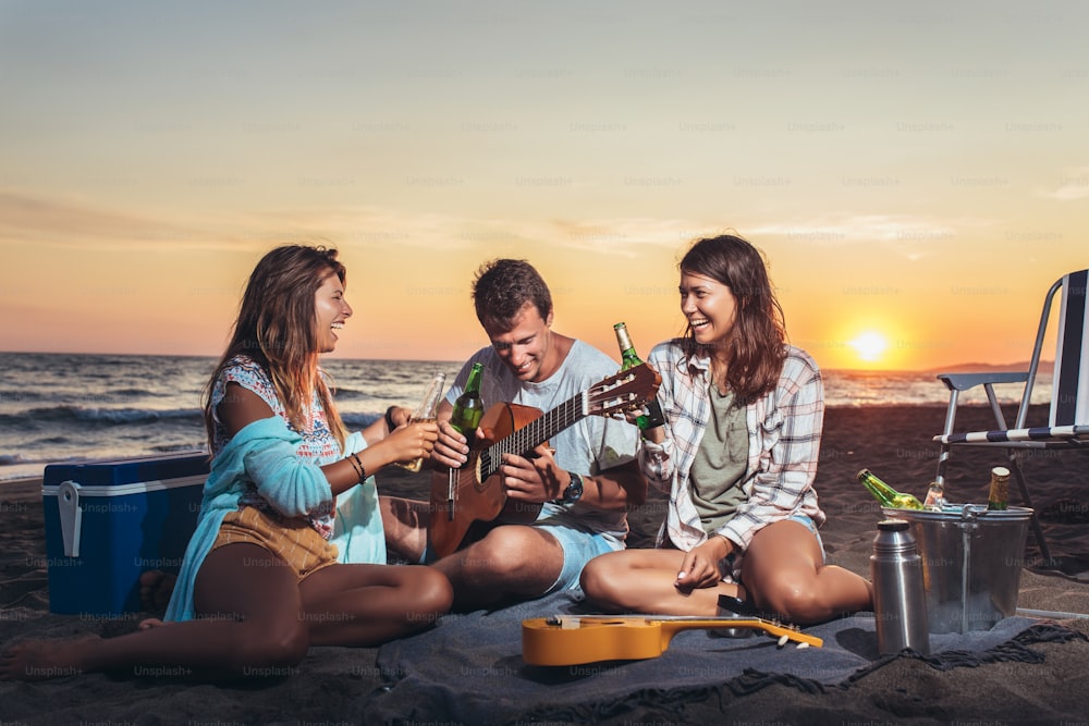 Gruppe von Freunden mit Gitarre, die sich bei Sonnenuntergang am Strand vergnügen.