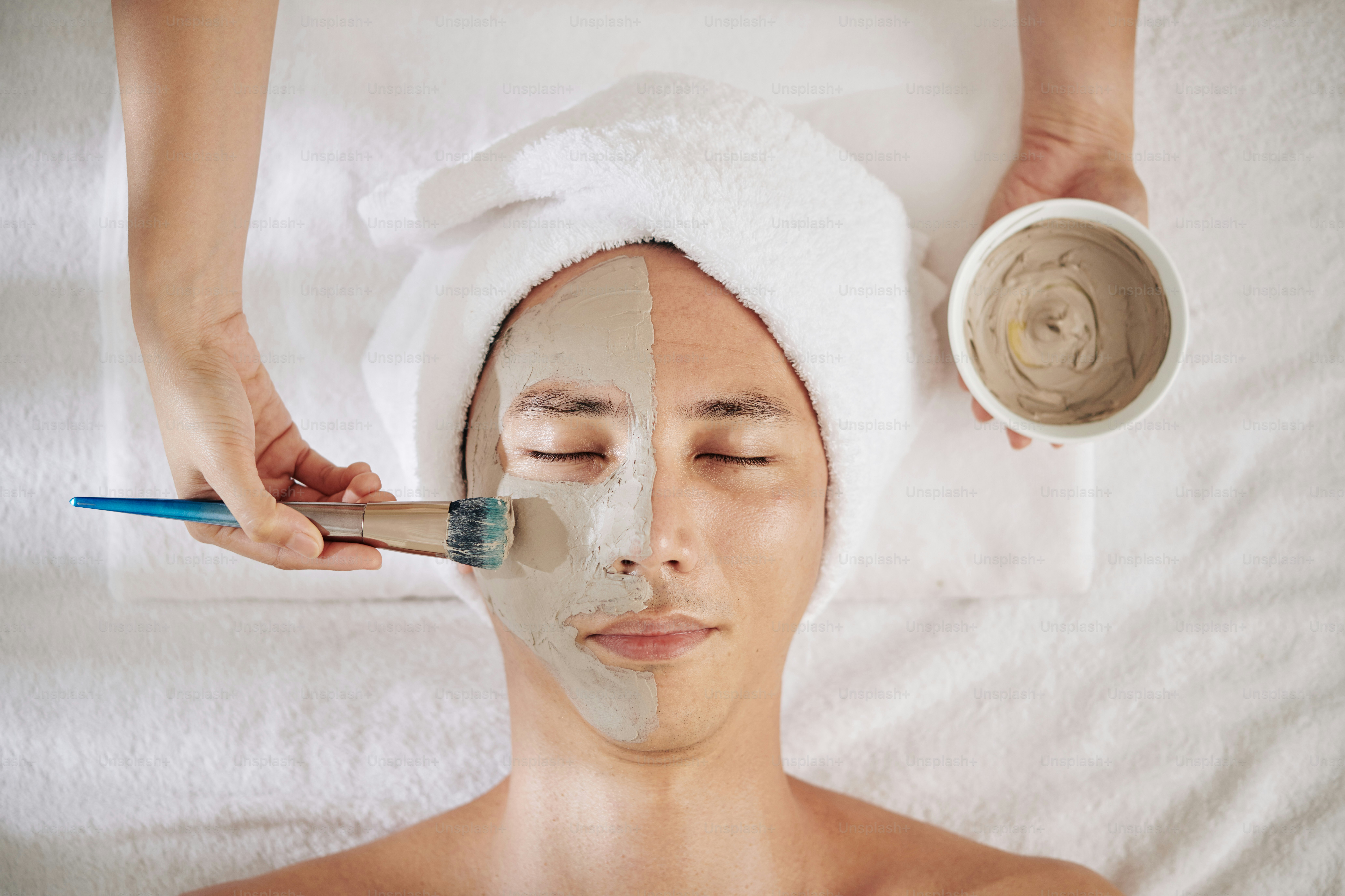 Giovane che ottiene la maschera di argilla anti-invecchiamento applicata sul suo viso nel salone di bellezza