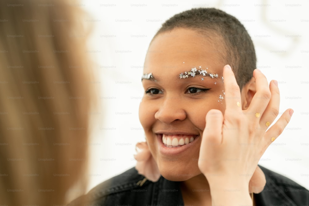 Close-up of woman applying star glitter on face of black woman while making makeup to her