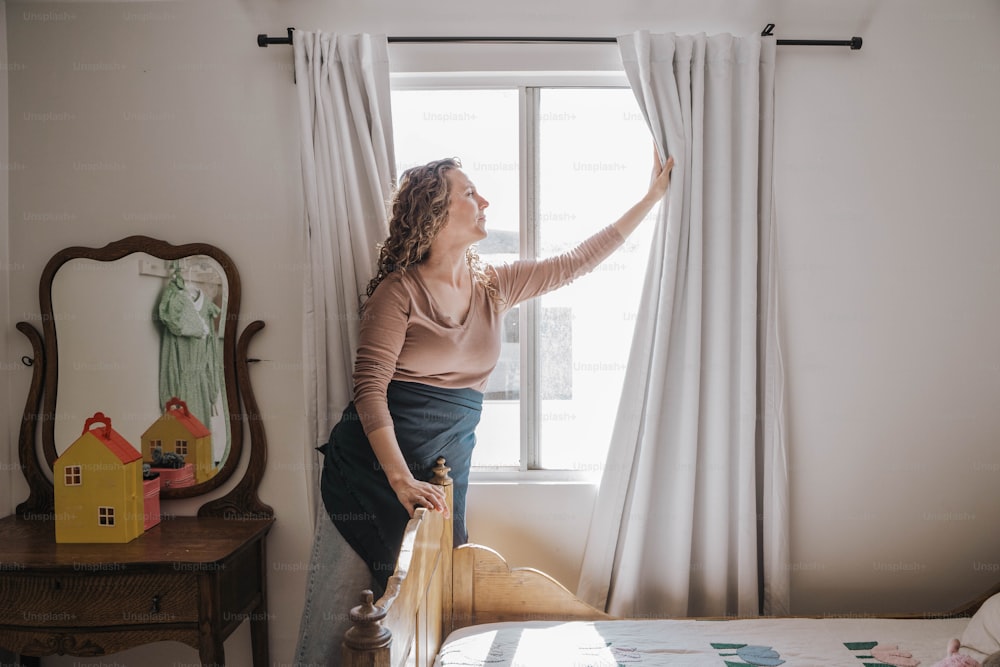 a woman standing next to a window in a bedroom