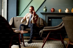 Handsome bearded businessman drinks coffee and making phone call in lobby