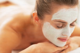 Mujer joven relajada con máscara revitalizante en la cara acostada en una mesa de masaje