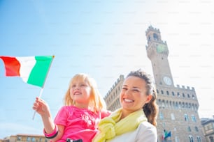 Madre feliz y niña con bandera frente al Palazzo Vecchio en Florencia, Italia