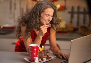 Happy young housewife with christmas snacks using laptop in kitchen