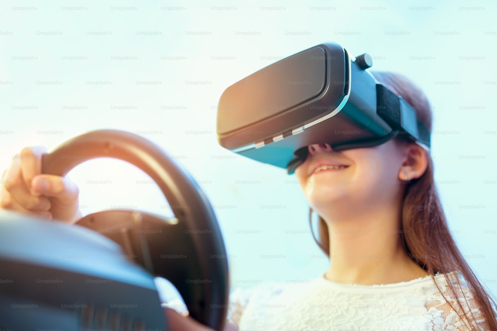 Happy girls in virtual reality glasses playing video game with racing wheels  at home