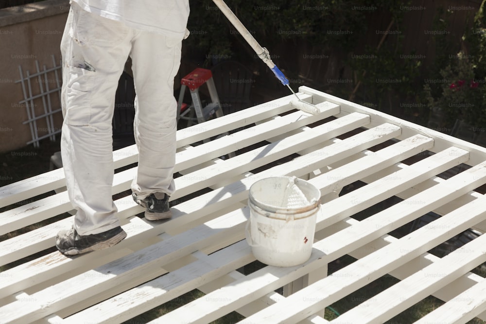 Painter Rolling White Paint Onto The Top of A Home Patio Cover.