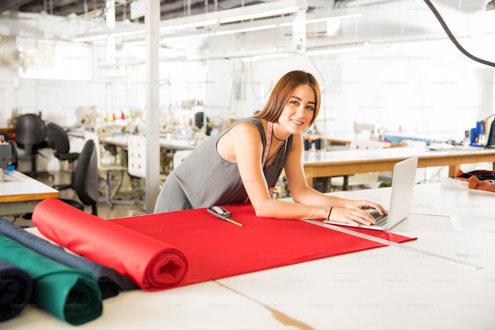 Young Hispanic fashion designer using a laptop computer in a textile factory