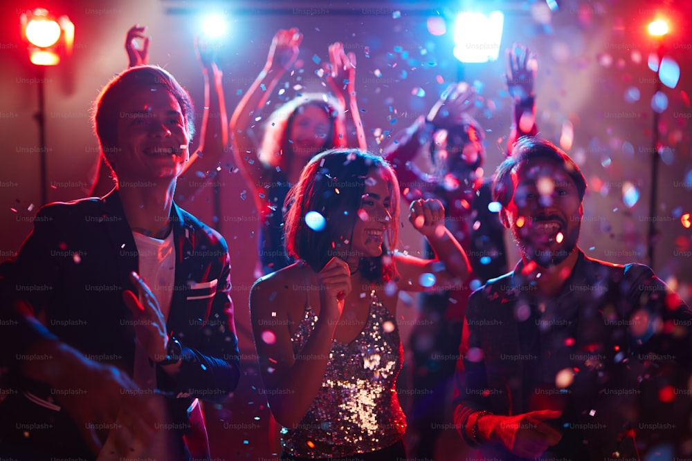 Jovens amigos felizes dançando em confetes durante a celebração do feriado