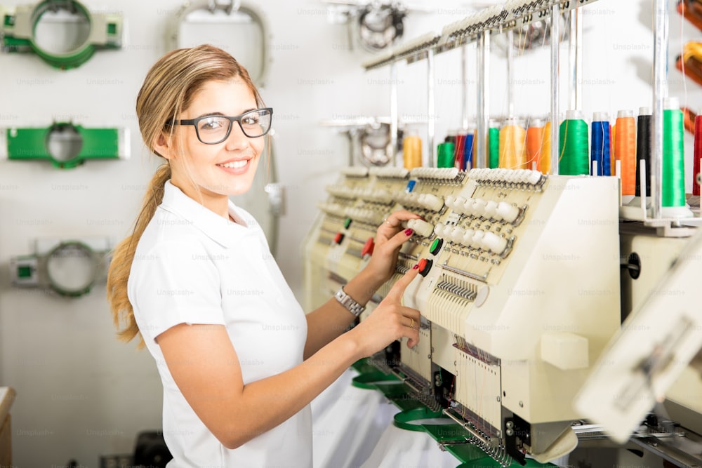 Profile view of a cute female worker setting up some thread rolls in an embroidery machine at a factory