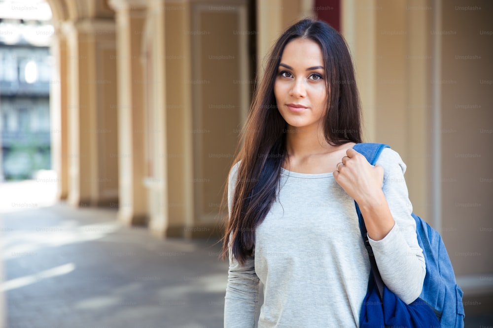 Portrait of attractive female student standing outdoors and lookign at camera