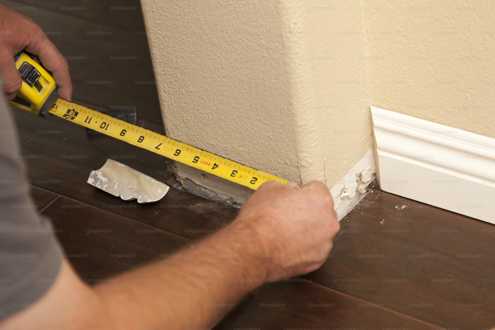 Contractor Measuring for New Baseboard with Bull Nose Corners and New Laminate Flooring Abstract.