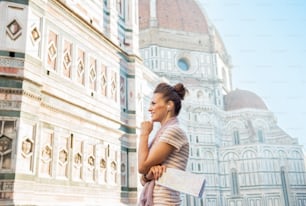 Glückliche junge Frau mit Karte und Audioguide vor der Cattedrale di Santa Maria del Fiore in Florenz, Italien