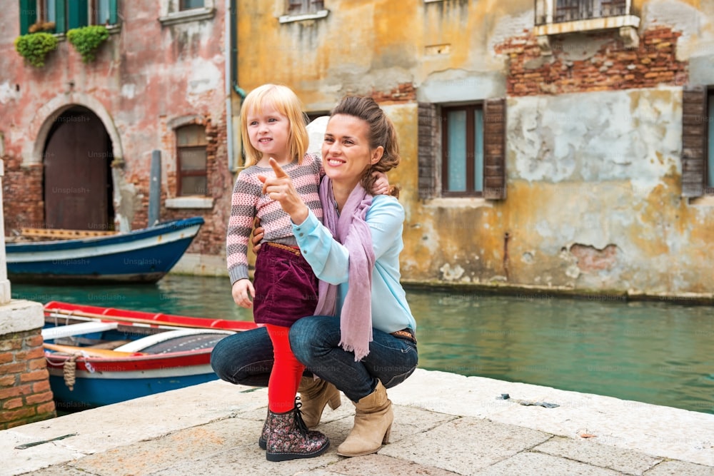 Baby girl and mother poiting on copy space while in venice, italy