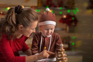 Happy mother and baby making christmas tree from cookies