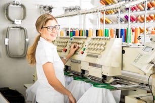 Attractive young Latin woman working with an embroidery machine in a factory and smiling