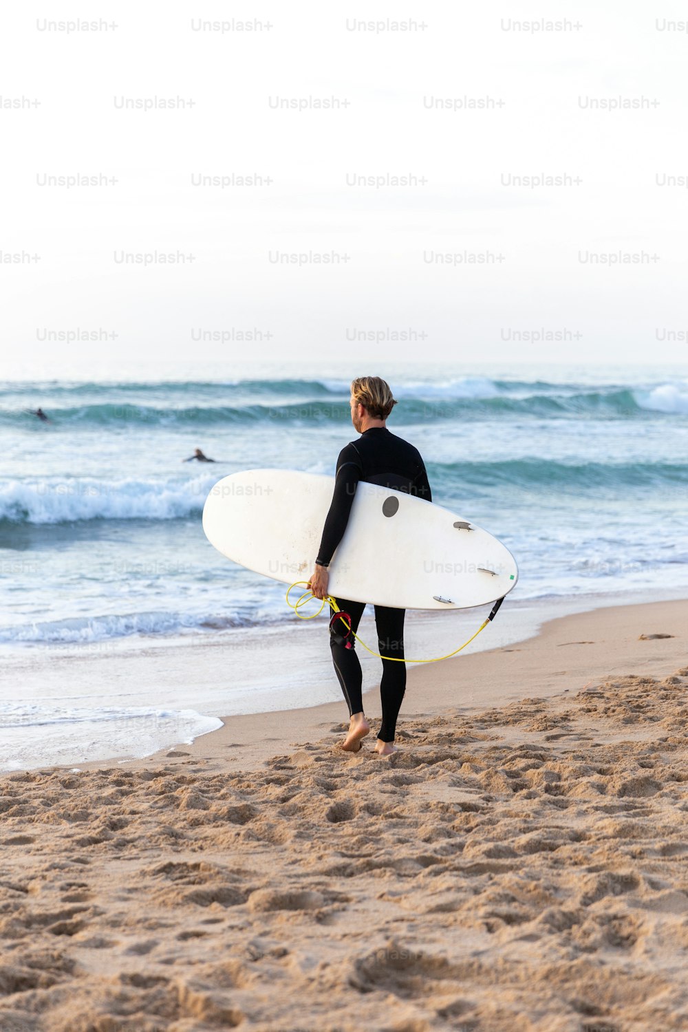 Un uomo in una muta che trasporta una tavola da surf su una spiaggia