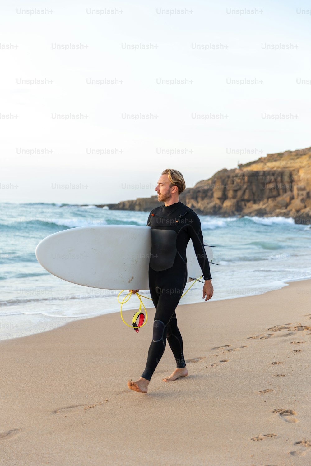 Un homme en combinaison de plongée portant une planche de surf sur une plage