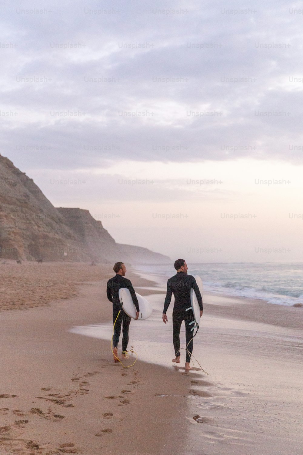 two surfers walking on the beach with their surfboards