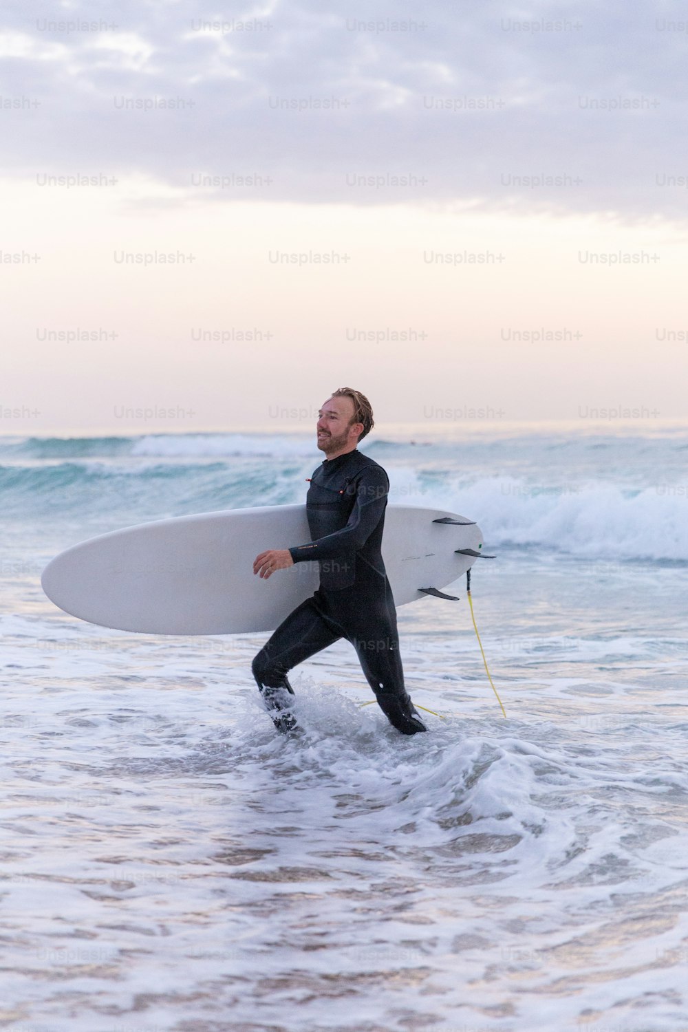 Un homme en combinaison de plongée transportant une planche de surf dans l’océan