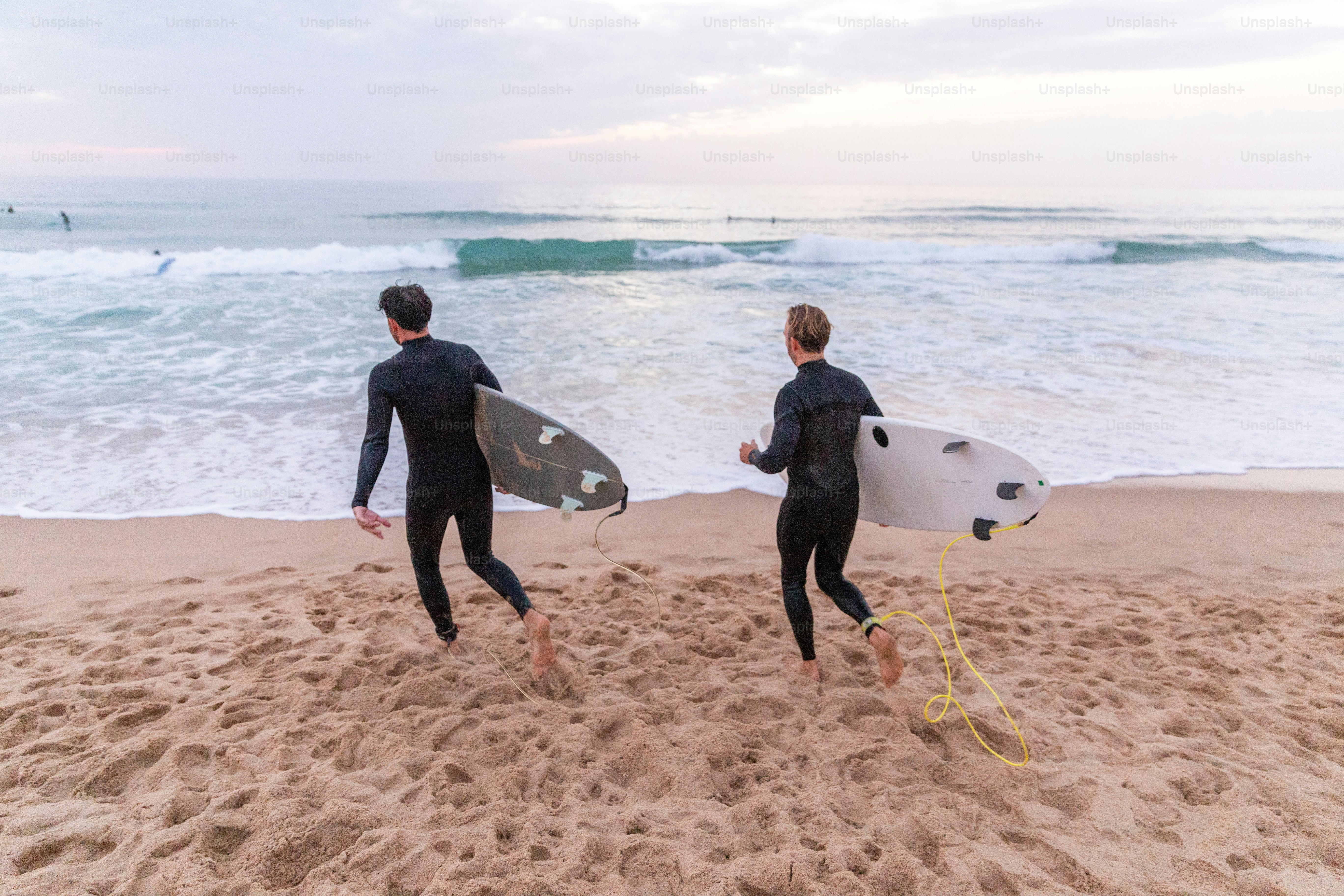 Zwei Männer in Neoprenanzügen, die Surfbretter am Strand tragen