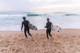 two men in wet suits carrying surfboards on a beach
