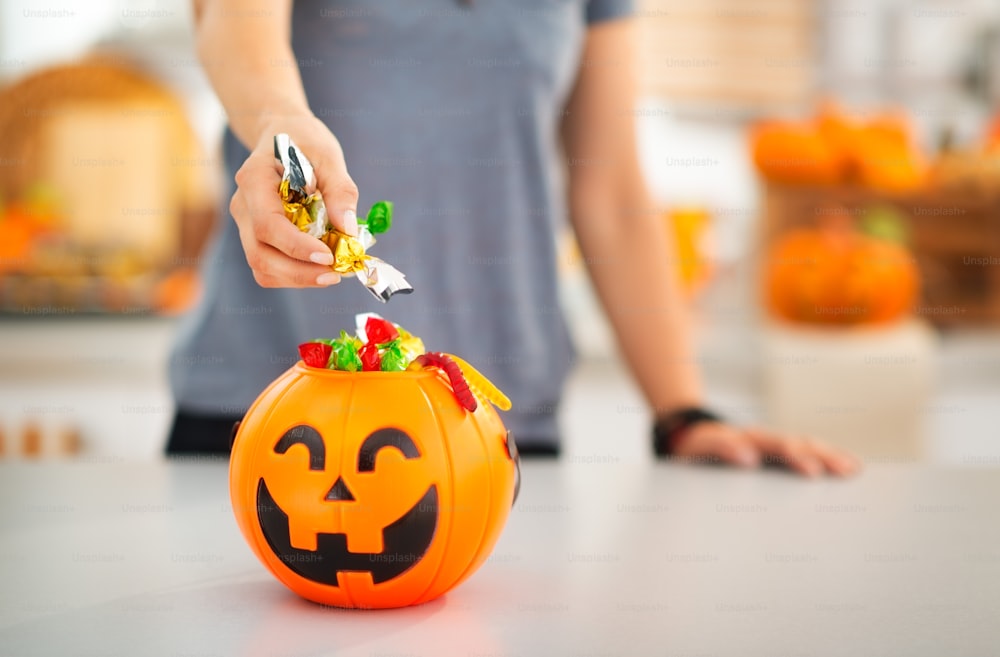 Doces de Halloween nunca são demais! Closeup na mulher colocando truque ou guloseimas doces no balde de halloween Jack-o-Lantern. Feriado tradicional de outono