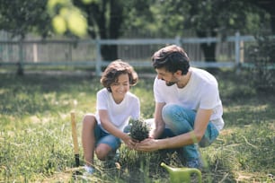 In the garden. Dark-haired boy and his dad holding the plant and talking
