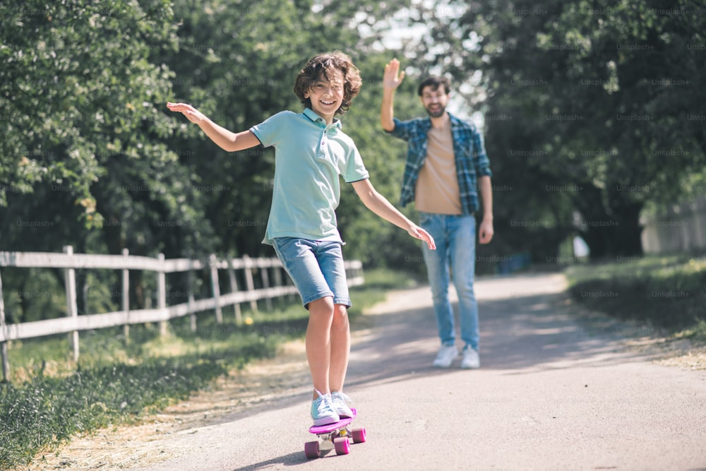 Riding a skateboard. Dark-haired boy riding a skateboard, his father watching him
