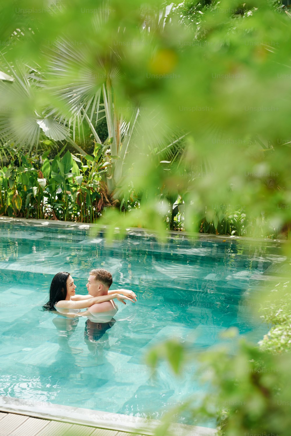 Young hugging couple spending hot summer day in refreshing water of swimming pool