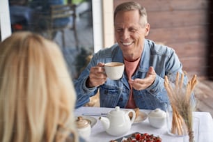 El hombre alegre está bebiendo té y comiendo bocadillos mientras habla con su esposa en la terraza de la casa del pueblo