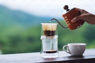 흐릿한 자연 배경으로 드립 커피를 만들기 위해 주전자에서 뜨거운 물을 붓는 손의 근접 촬영 이미지