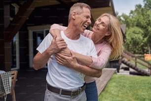 Porträt einer glücklichen Frau, die ihren Ehemann umarmt, während sie im Hof eines Landhauses stehen