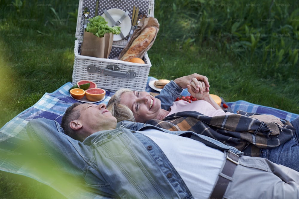 Una pareja madura feliz está acostada en la hierba y abrazándose después de comer comidas saludables en madera verde