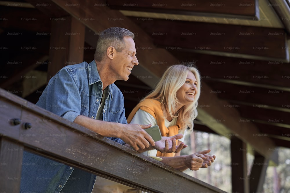 Niedriger Winkel des lächelnden reifen Mannes mit Smartphone und Frau, die Urlaub im Ferienhaus verbringt